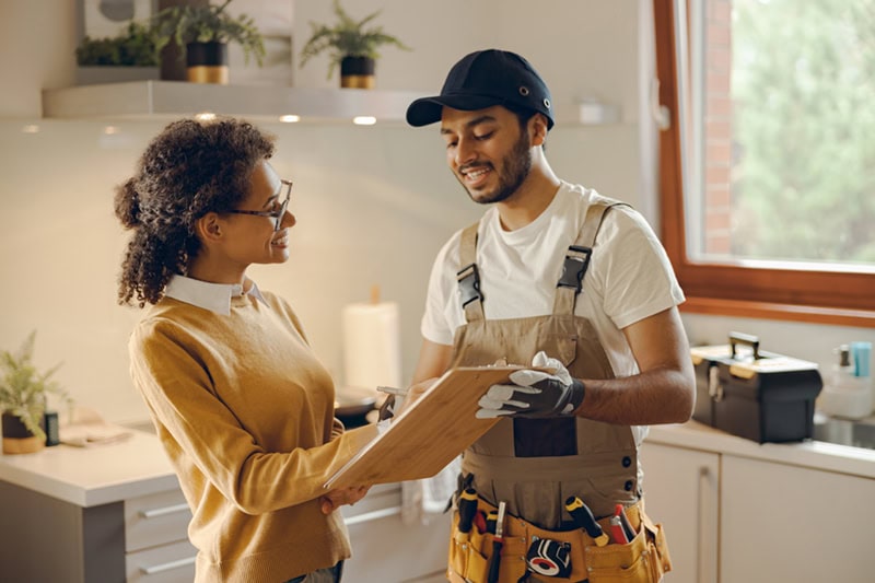 A friendly interaction between a female homeowner and a service technician inside a kitchen.